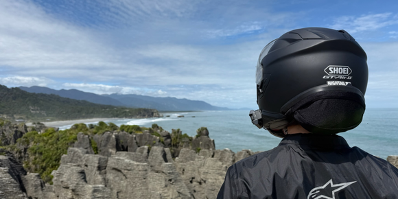 Motorcyclist wearing a helmet with a Hightail on it looking at the coast